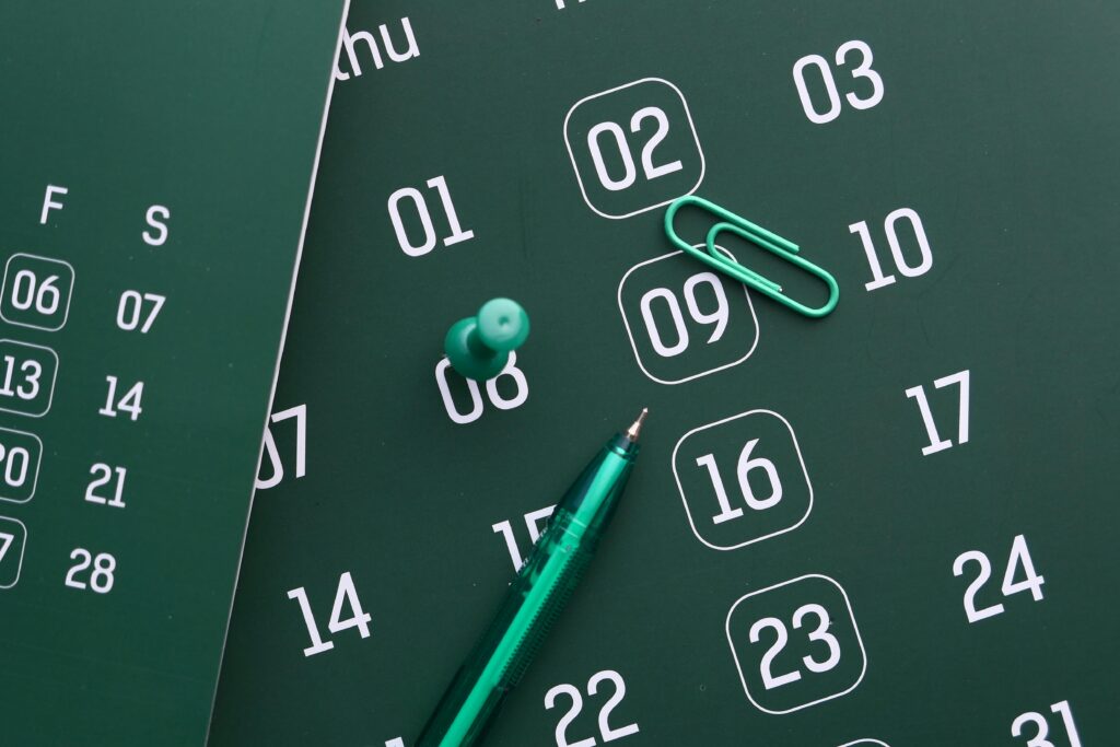 Close-up of a green calendar with pen, push pin, and paper clip for planning and organization.